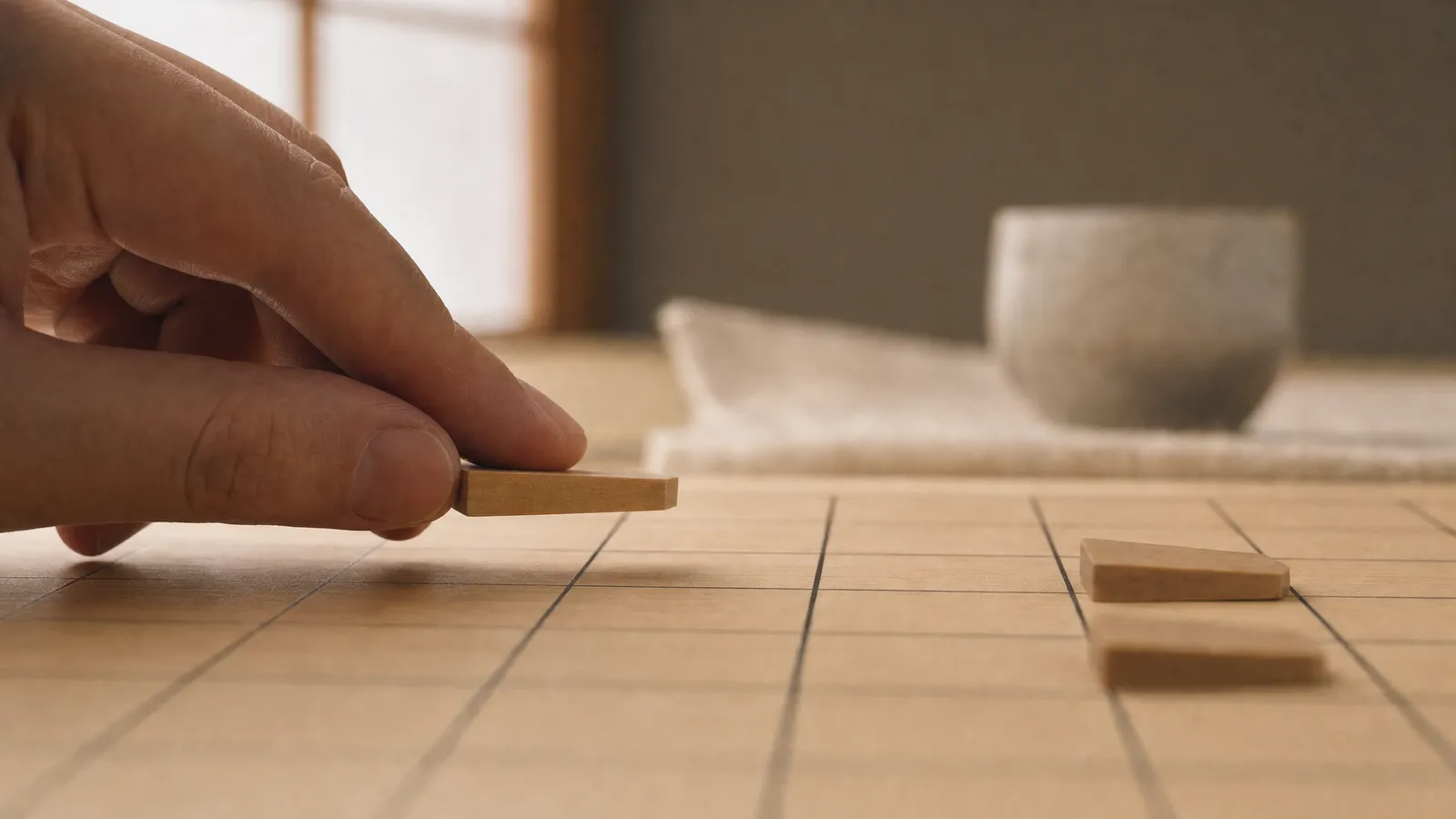 Fingers lowering a flat wooden piece onto an empty square of a shogi board, two pieces ahead, a classic shogi tesuji drop